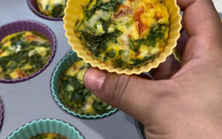 Hand holding yellow silicone egg muffin cup with spinach and tomato, baked in muffin tin