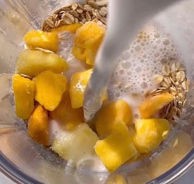 Milk pouring into blender with frozen mango chunks and oats for smoothie prep